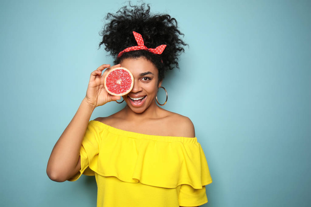 Portret van de jonge Afro-Amerikaanse vrouw met grapefruit op kleur achtergrond - Foto, afbeelding