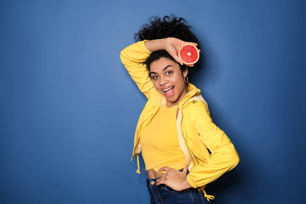 Portrait of young African-American woman with grapefruit on color background - 写真・画像