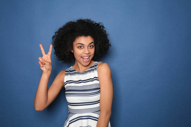 Portrait de jeune femme afro-américaine montrant un geste de victoire sur fond de couleur
 - Photo, image