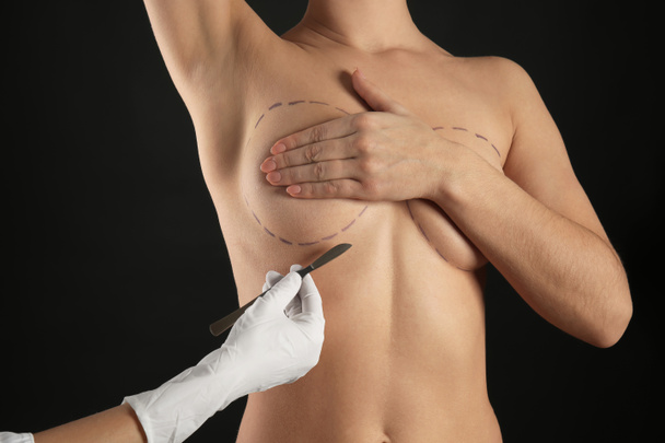 Naked woman and doctor's hand with lancet on dark background. Concept of breast augmentation - Photo, Image