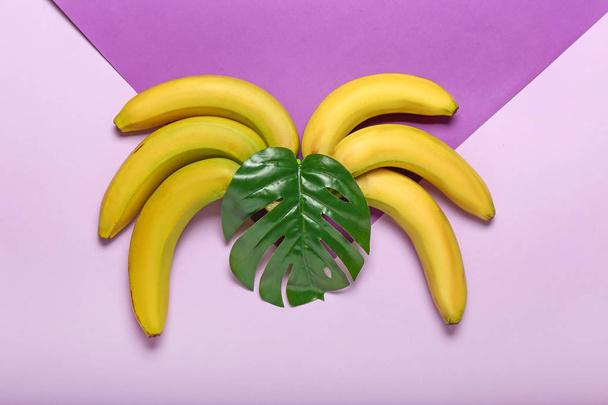 Ripe sweet bananas and tropical leaf on color background - Photo, Image