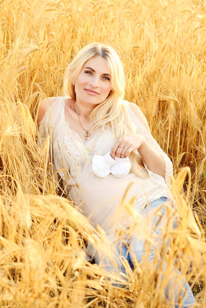 mujer embarazada que pone en el campo de trigo con bootee en la panza
 - Foto, imagen