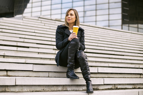 Beautiful businesswoman enjoys resting outdoor at the city and drinking coffee.Toned image. - Valokuva, kuva