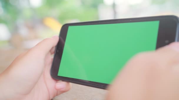 若いアジアの女性は、緑色の画面で黒の携帯電話のデバイスを使用します。カフェで座っている間ページをスクロールするスマート フォンを保持しているアジア女性。クロマ キー. - 映像、動画