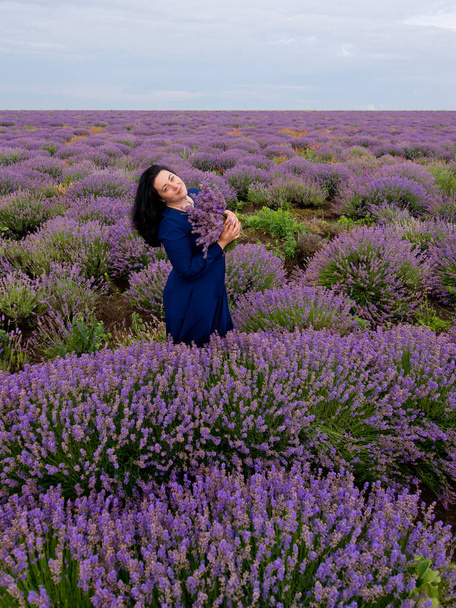 Young girl with a bouquet in hands, posing in a lavender field. - Foto, afbeelding