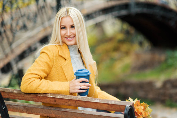 Young stylish blond woman drinking coffee to go in a park  - Foto, Imagen