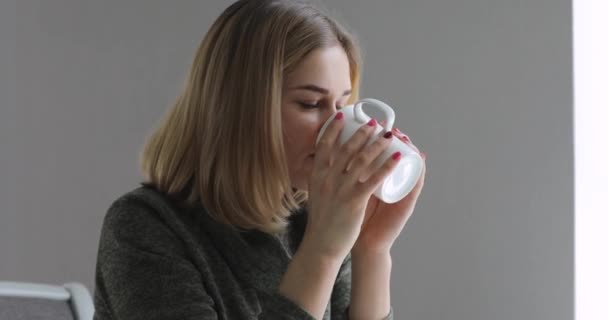 Young woman drinking tea at home window - Felvétel, videó