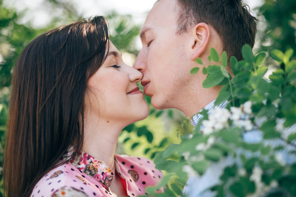 Krásný mladý pár, jemně objímání a líbání v zelené listy a bílé květy v jarní zahradě. Šťastná rodina zahrnující na kvetoucí akát strom ve slunečním světle. Romantické chvíle - Fotografie, Obrázek