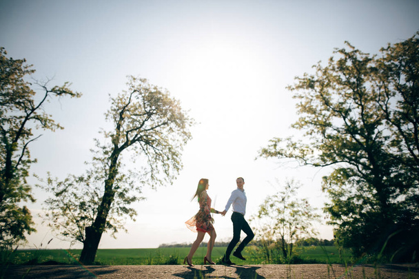 Beautiful young couple holding hands and running in sunshine in spring field and trees. Silhouettes of happy family having fun  in sunlight. Romantic joyful moments. Space for text - Photo, Image
