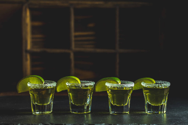 Mexican Gold Tequila shot with lime and salt on black stone table surface, selective focus, shallow depth of the field, copy space. - Photo, Image