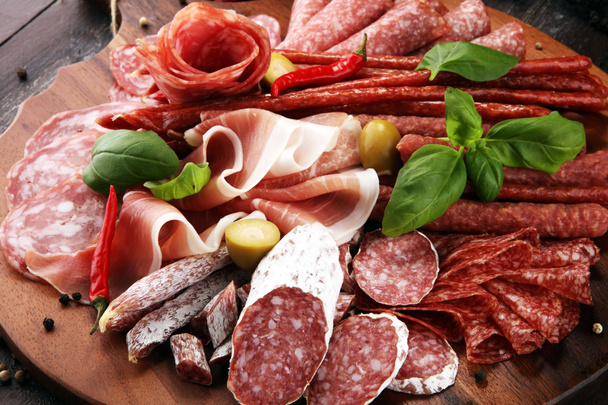Food tray with delicious salami, pieces of sliced prosciutto crudo, sausage and basil. Meat platter with selection. - Photo, Image