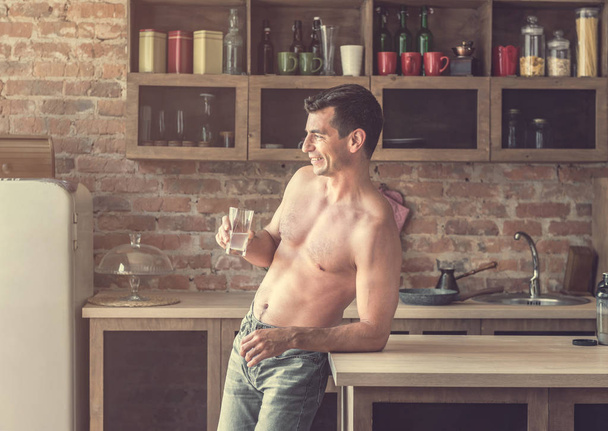 athletic man drinks water with lemon in the kitchen - Фото, зображення
