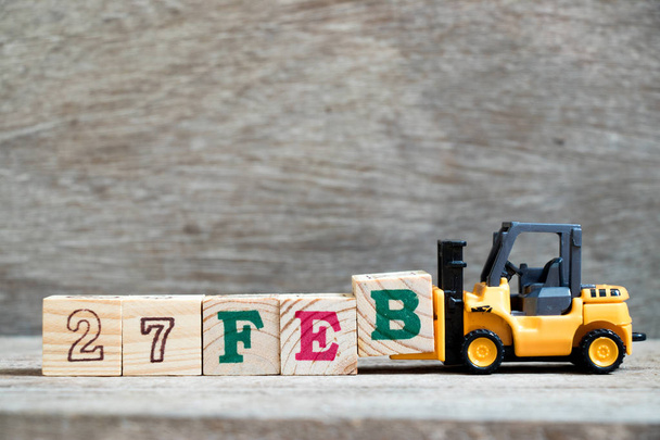 Toy forklift hold block B to complete word 27feb on wood background (Concept for calendar date 27 in month February) - Photo, Image