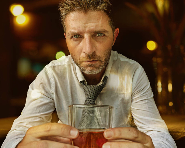 young attractive and depressed alcohol addict man in lose tie drunk and wasted at bar pub late night drinking whiskey glass in alcoholic businessman and alcoholism problem concept - 写真・画像