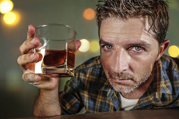 young sad and depressed alcoholic man with whiskey glass wasted and drunk failing resisting to drink in bar pub at night falling into alcohol abuse in addiction and alcoholism problem  - Photo, image