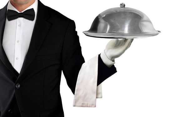 Ober in tuxedo holding dienblad met metalen cloche en servet op witte achtergrond - Foto, afbeelding