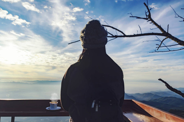 Una viajera bebe café en el restaurante con vistas al paisaje de montaña. Una joven turista bebe una bebida caliente de una taza y disfruta del paisaje en las montañas. Concepto de trekking - Imagen
 - Foto, imagen