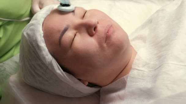 Modern cosmetology procedure for cleansing and rejuvenation of the skin. Darsonvalization. Hardware cosmetology. A girl of Asian appearance in a beauty salon. - Footage, Video