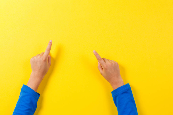Kid hands pointing to something on yellow background. - Foto, immagini