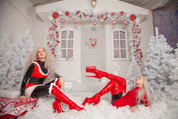 two bad Santa's girlfriends in latex costumes play in the front yard of their house at Christmas - Photo, Image