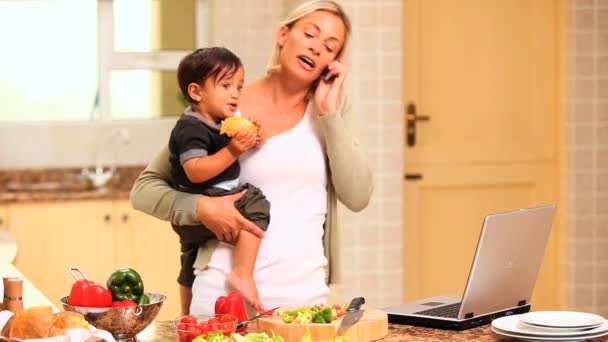 Woman in kitchen coping with baby and laptop and phone - Footage, Video