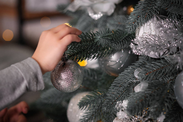 Close-up of child hanging decorative toy ball on Christmas tree branch - Фото, изображение