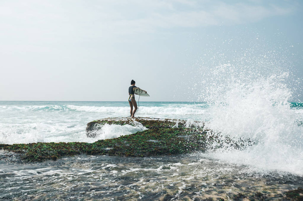 Woman surfer with surfboard going to surf on mossy seashore coral reefs - 写真・画像