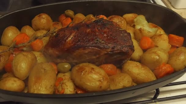 Filming hot freshly roasted meat loaf with potatoes ,carrots and olives. Young potatoes with meat in iron pan just taken out of oven still smoking in slow motion hd. - Footage, Video