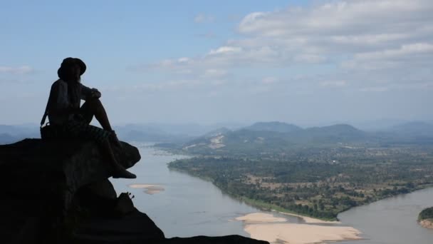 Asian thai woman travel visit and posing sitting on ridge stone of cliffs at Wat Pha Tak Suea temple with view of landscape of Nongkhai city and loas and Mekong river in Nong Khai, Thailand - Footage, Video