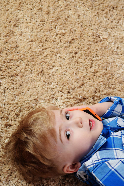 小さな男の子はカーペットの上で横になっている、携帯電話で再生します。スマート フォンを使用して小さな男の子。技術コンセプト. - 写真・画像