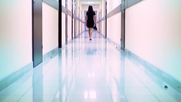 Vista posteriore di una donna in abito nero che cammina lungo il corridoio dell'hotel. Lei sta tenendo le scarpe in mano
 - Filmati, video