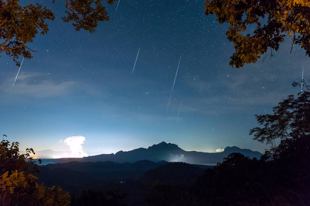 Meteorický roj Geminidy na noční obloze s mlhou na kopci, dlouhé expozice, Mae Moh Lampang, Thajsko. - Fotografie, Obrázek