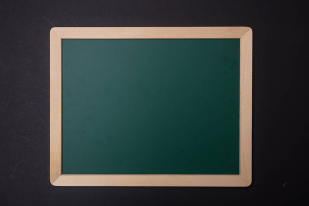 Green blank empty chalk board with wooden frame, black wall background. Space for text - Photo, Image