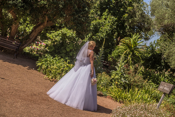 Noiva em belo vestido de noiva branco em pé no jardim de flores trópicas. Tiro no casamento na Austrália na praia de areia incrível
. - Foto, Imagem