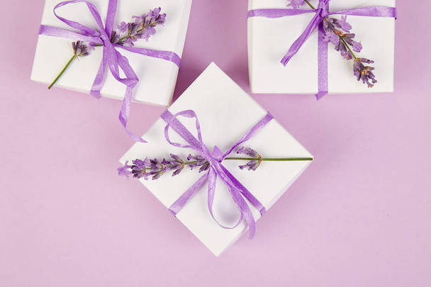 Confezione regalo bianca con nastro viola e bouquet di fiori di lavanda su sfondo rosa. Celebrazione, compleanno. Regalo di decorazione. Piatto. Copia spazio
. - Foto, immagini