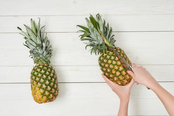 cropped view of woman cutting ripe pineapple with knife  - Zdjęcie, obraz