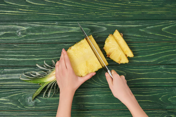 vista cortada de mulher cortando amarelo abacaxi maduro na mesa de madeira verde
 - Foto, Imagem