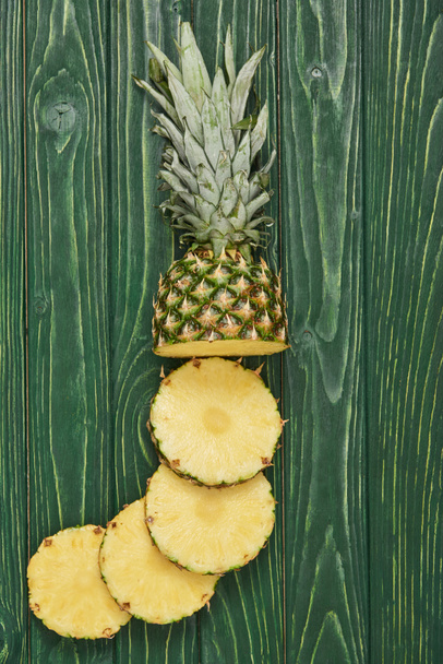 top view of sliced circles of tasty pineapple on green wooden table - 写真・画像
