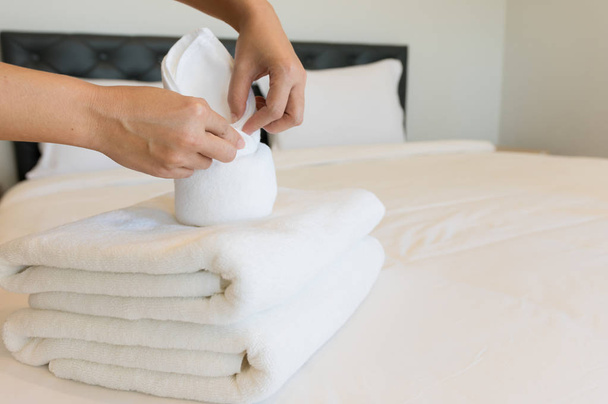 Nuori hotellineito laittaa pehmeitä pyyhkeitä hotellihuoneeseen. pyyhkeet asetettiin puhtaalle valkoiselle peitteelle sängylle tyynyllä makuuhuoneessa aamulla
. - Valokuva, kuva