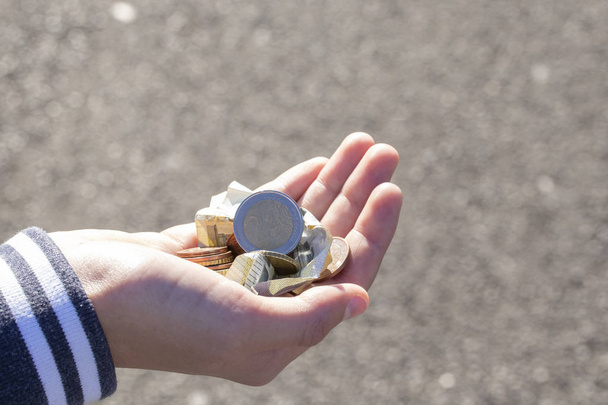 Ребёнок держит в руках монеты и банкноты евро. Карманные деньги. Бедная семья с низкими доходами, понятие бедности, попрошайничество
 - Фото, изображение