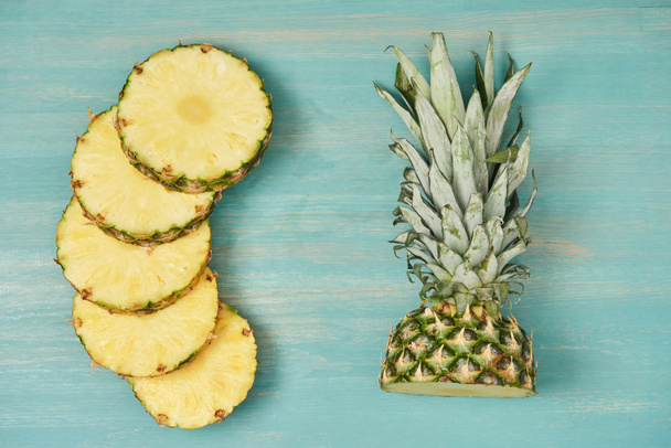 pohled shora plátky kruhů a řez ananasu na tyrkysové dřevěný stůl - Fotografie, Obrázek