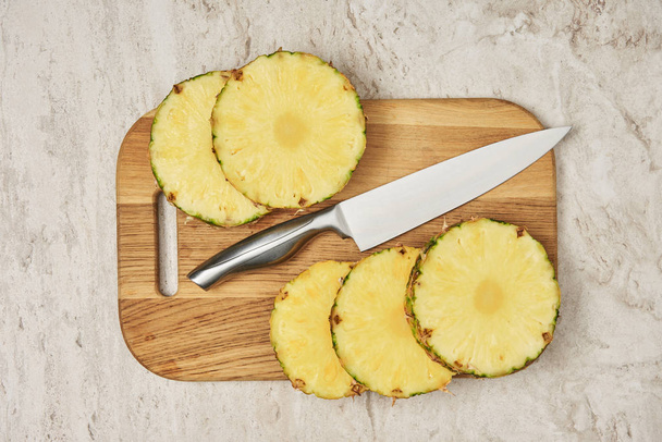 vue du dessus des cercles d'ananas tranchés sur une planche à découper en bois près d'un couteau
  - Photo, image