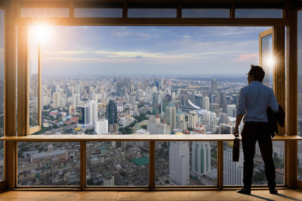 Concept vision, Young businessman wearing comfortable casual suit standing in Working room near the glass window and looking through the modern buildings in the skyline. - Zdjęcie, obraz