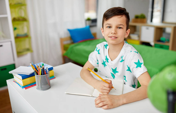 ευτυχισμένο αγόρι γράφοντας ή σχεδιάζοντας στο σημειωματάριο στο σπίτι - Φωτογραφία, εικόνα