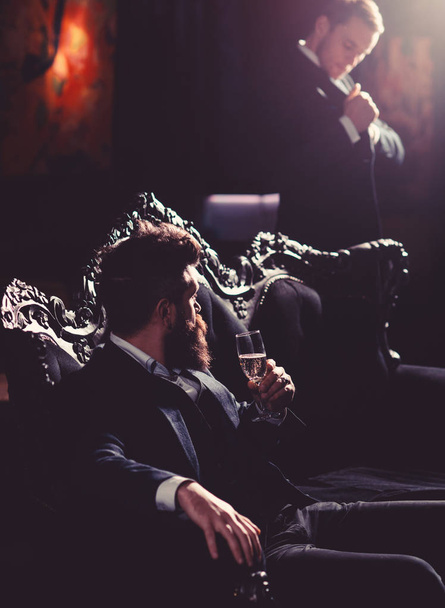 Alcohol, wealthy lifestyle, business, money concept. Boss in luxury suit sits on vintage sofa. Mature man with beard talks to assistant. Bearded man with serious face and champagne glass - Valokuva, kuva