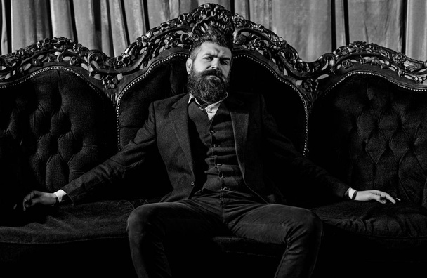 Millionaire in elegant suit sits on luxurious sofa. Bearded man with confident face in classic interior. Luxury lifestyle, confidence, success, rich, power, fashion, wealth, furniture, concep - Photo, Image