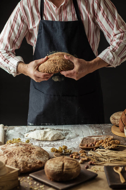 Unrecognizable baker holds freshly baked rustic organic loaf of bread in hand - Fotoğraf, Görsel