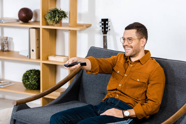 handsome man sitting on sofa and holding remote control  - Фото, зображення