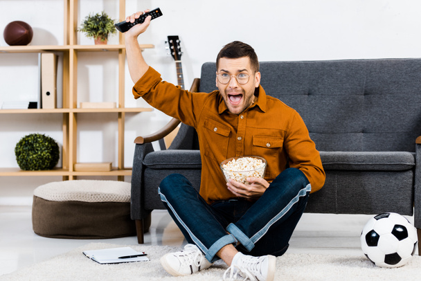 excited man holding bowl with popcorn and screaming at home - 写真・画像