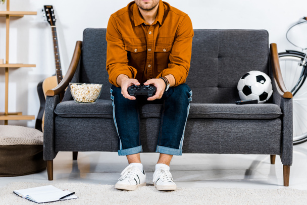 oříznutý pohled člověka sedí na pohovce a hrát video hry - Fotografie, Obrázek